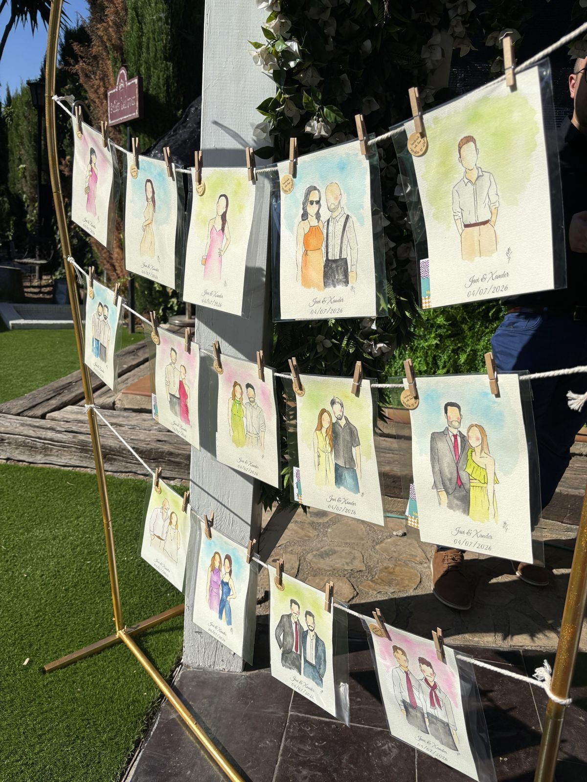 Acuarelas de invitados colgadas con pinzas en un arco dorado durante una boda